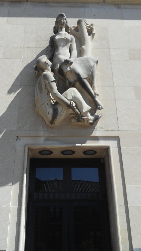 #SilentSunday photo of bas relief  sculptures of one human figure looking up at another seated human displayed over a post office entrance.
